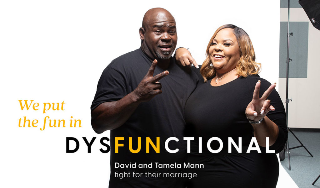David and Tamela Mann standing side by side smiling and holding up peace signs.