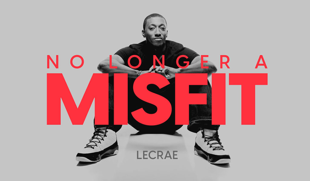 Lecrae sitting on the ground with his knees up and arms resting on them.