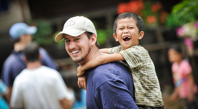 A man in a hat with a young child riding on his back smiling.