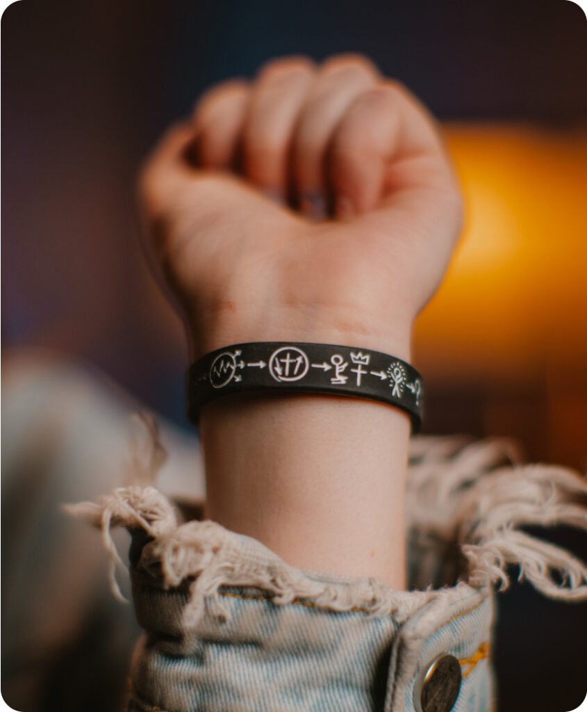 A close-up of someone wearing a frayed denim jacket with a 3 circles wristband on.
