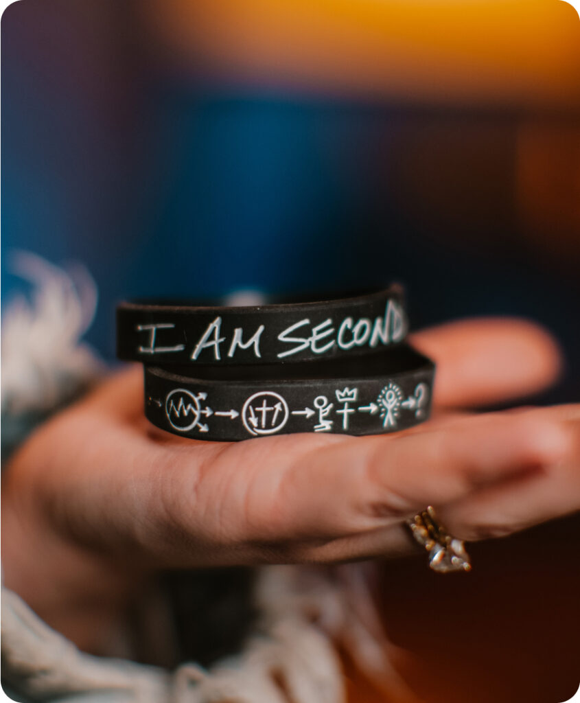 A close-up of a woman's open hand holding 2 I Am Second 3 circles wristbands in her open palm.